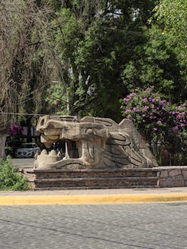 Ancient stone serpent sculpture in Teotihuacán, México, surrounded by lush greenery and vibrant flowers.