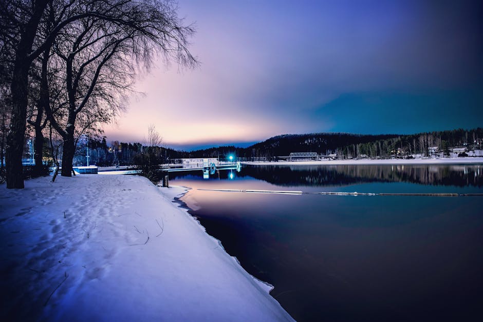 Peaceful winter evening scene in Jyväskylä, Finland, featuring calm frozen lake and snow-covered trees.