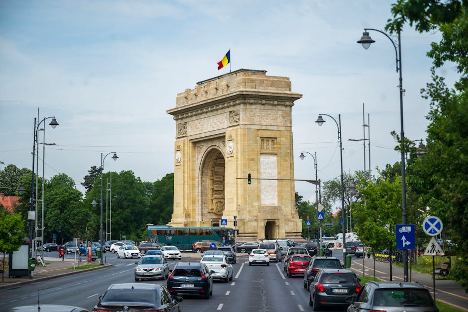 View of traffic at the historic Arcul de Triumf in Bucharest, Romania with cars and bright daytime setting.