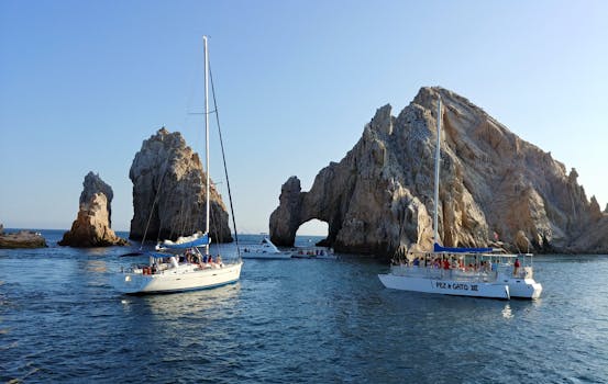 Beautiful sailboats near the iconic Arch of Cabo San Lucas, Mexico under a clear blue sky.