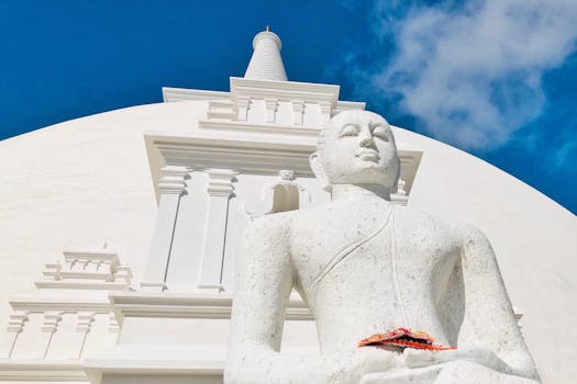 Low angle view of a Buddha statue at a stupa in Anuradhapura, Sri Lanka, under a clear blue sky.