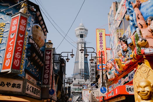 Lively street view in Osaka with vibrant shops and the iconic Tsutenkaku Tower in the background.