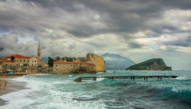 Historic Budva coastline with medieval architecture and rugged sea under dramatic skies.