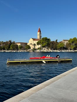A picturesque view of Trogir Cathedral from a marina with clear blue skies.