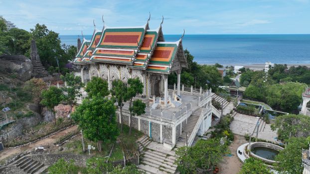 A stunning aerial shot showcasing a traditional Thai temple near the coastline with a view of the sea.