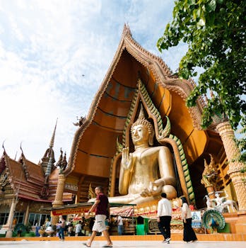 A magnificent golden Buddha statue at Wat Tham Sua in Kanchanaburi, Thailand, under a clear sky.